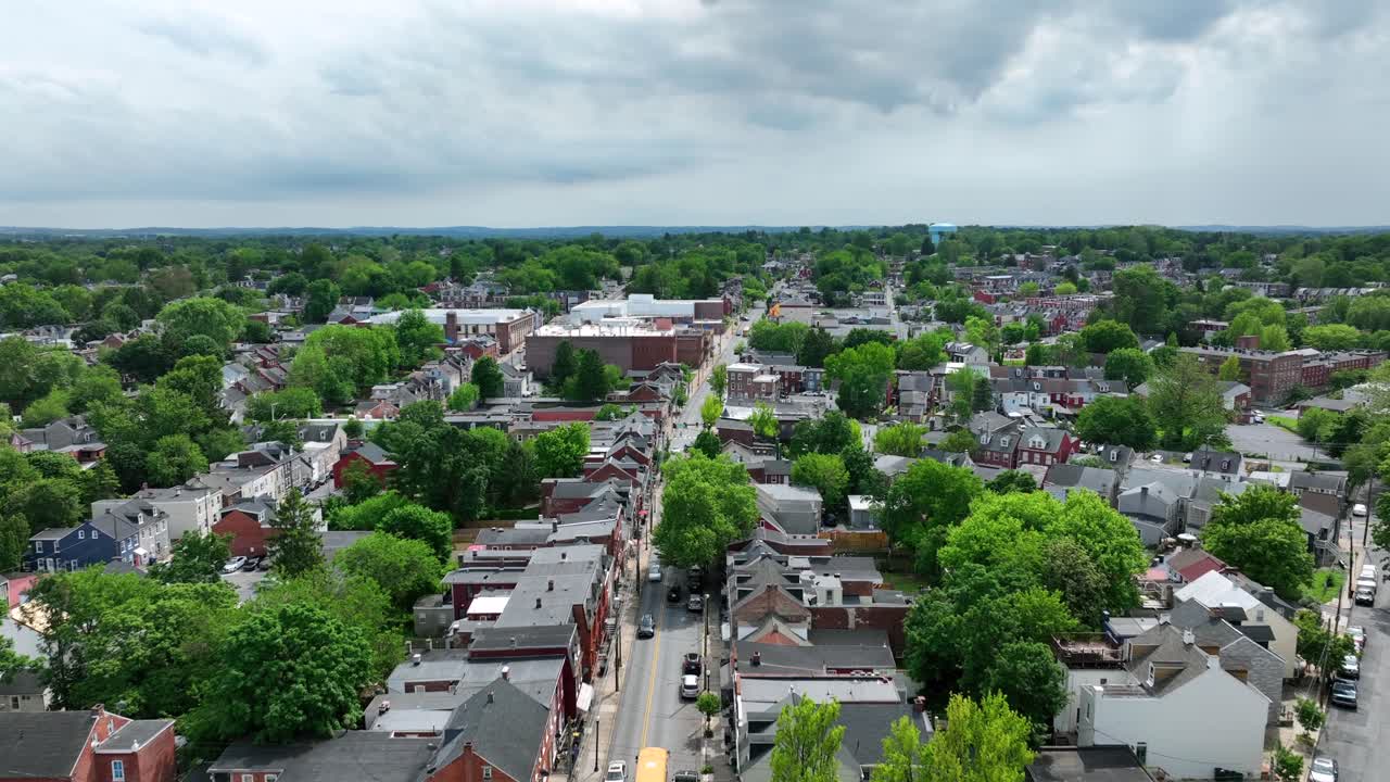 Aerial view of yellow american school bus on Main Street of town.Green spring trees during cloudy day in Lancaster, PA, USA. Wide shot. Historic buildings and houses in City.
