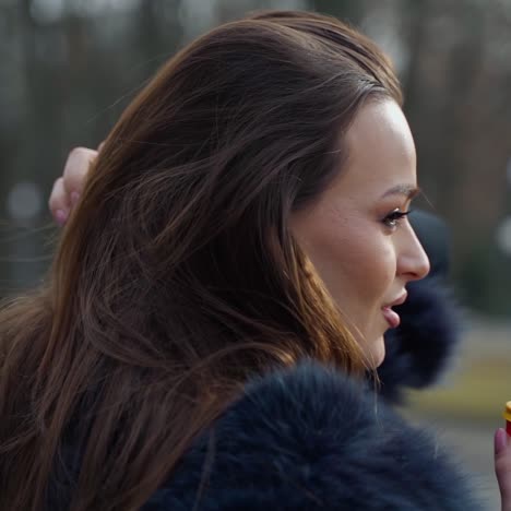 profile of a beautiful woman in winter. attractive brunette with long hair holds plastic cup with hot beverage outdoors. slow motion.