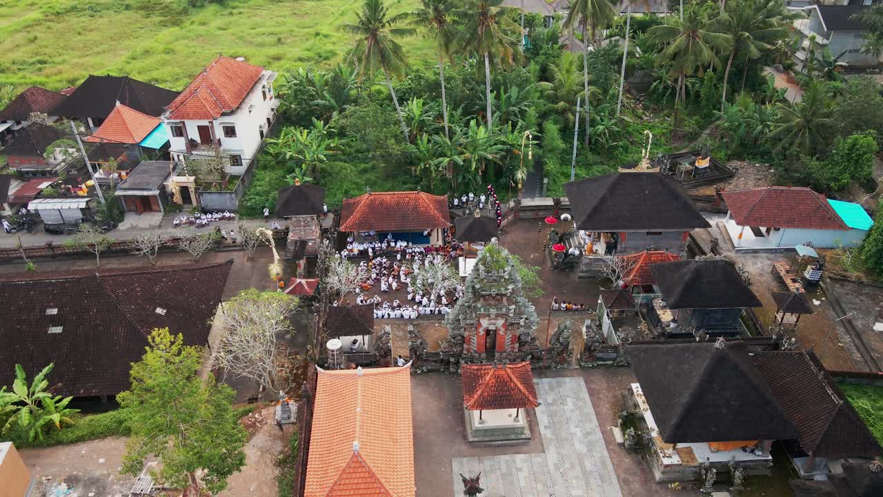 Aerial footage zooms out from a temple during a ceremony, as Hindu locals pray in the temple in Ubud village, Bali. Surrounded by lush greenery and rice fields as the backdrop.