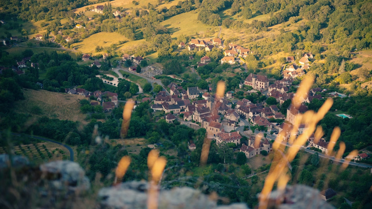 Scenic high angle view of Autoir village nestled in a green valley during golden hour. Historic French architecture surrounded by lush nature in Lot region of France with blurred foreground grass.
