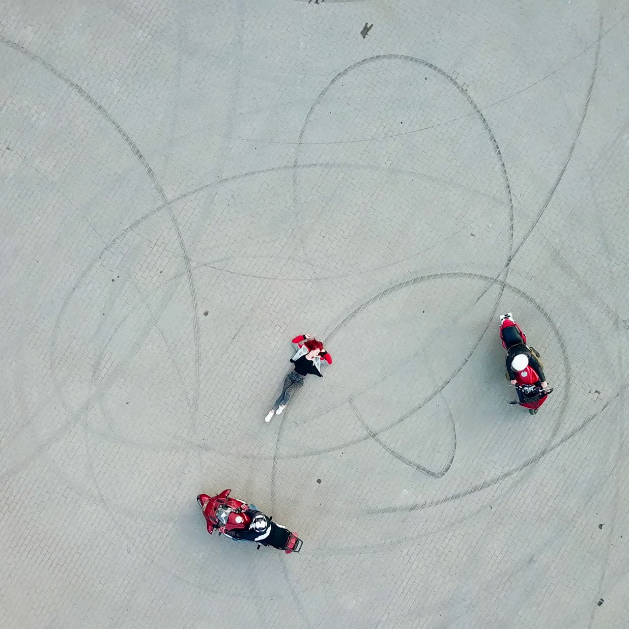 Top view of two professional bikers racing slowly in a circle way. Young woman is lying in the middle of a road and two motorcycles riding around her. Dangerous sport. Aerial view.