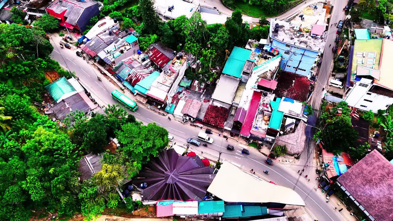 A vivid aerial shows a Sri Lankan village with tightly packed colorful rooftops, winding roads, and surrounding lush greenery, blending rural charm with lively human patterns.