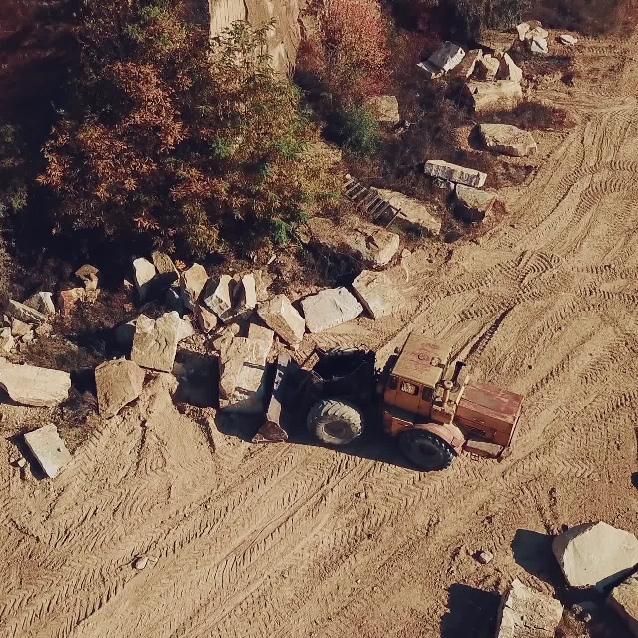 specially equipped bulldozer with a jug is picking up a stone in the quarry on the background of a rock with a forest. View of the sand quarry. Camera motion up.