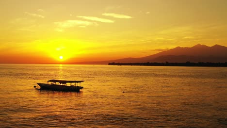 Red-and-yellow-sunset-with-small-fishing-boats-and-mountains-in-the-background-across-a-large-body-of-water