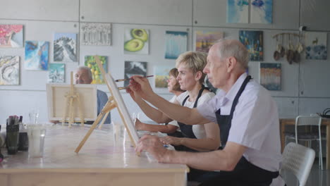 the teacher shows a group of friends of retired people in the elderly at drawing courses. a group of elderly men and women draw together and smile