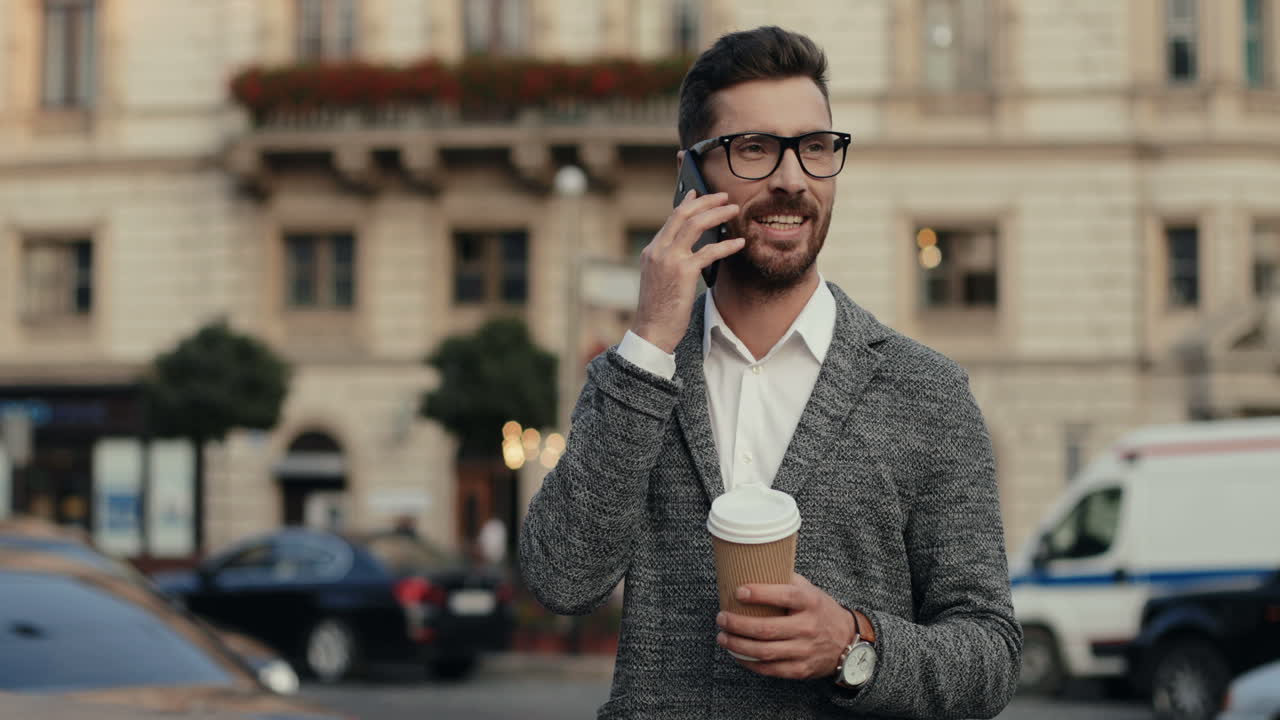 hombre de negocios con estilo en gafas de pie en la calle, hablando por teléfono y tomando café