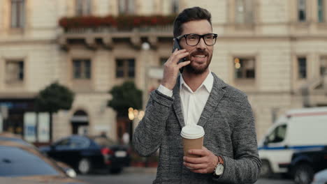 Stylish-Businessman-In-Glasses-Standing-In-The-Street,-Talking-On-The-Phone-And-Drinking-Coffee
