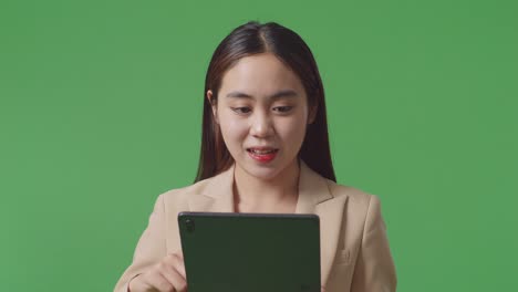 close up of asian business woman smiling while using tablet on green screen background in the studio