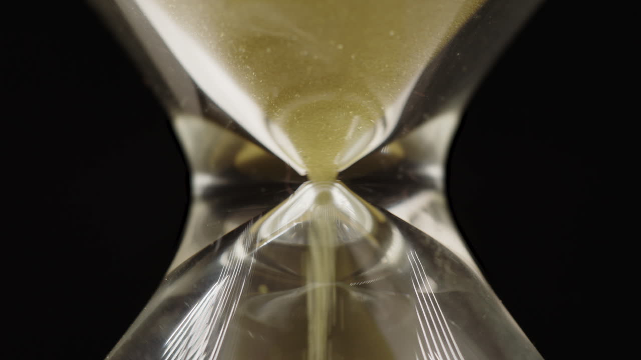 Extreme closeup of yellow sand passing through an hourglass, stress, urgency