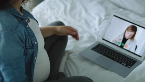 tilt down video of pregnant woman talking with doctor online.