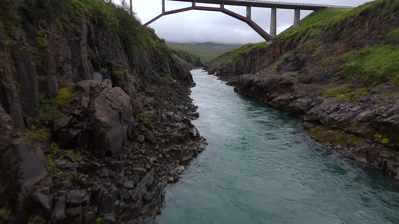 Aerial view of the Jökulsá River bridge in Iceland, showing flowing water, surrounding rugged terrain, and wide open landscape under clear sky