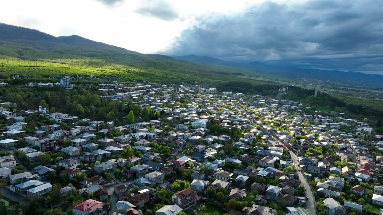 Ripresa aerea con drone di una città storica europea caratterizzata da architettura tradizionale, un campanile e verdi colline circostanti. Il cielo spettacolare e la luce naturale esaltano l'atmosfera cinematografica.