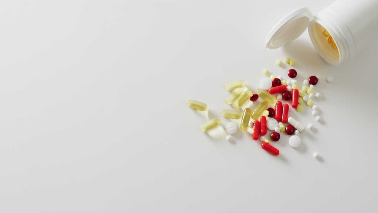 video de una caja blanca de pastillas derramando una variedad de pastillas y cápsulas sobre un fondo blanco con espacio para copiar.