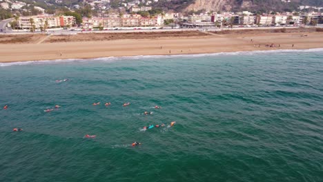 Schwimmer-Im-Meer-In-Der-Nähe-Des-Strandes-Von-Castelldefels-In-Barcelona,-Küstenstadtbild-Im-Hintergrund,-Tagsüber,-Luftaufnahme