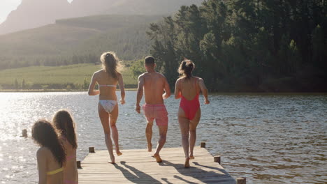 Amigos-En-Cámara-Lenta-Saltando-Del-Embarcadero-En-El-Lago-Al-Atardecer-Divirtiéndose-Chapoteando-En-El-Agua-Disfrutando-De-La-Libertad-Compartiendo-Aventuras-De-Verano-En-Vacaciones