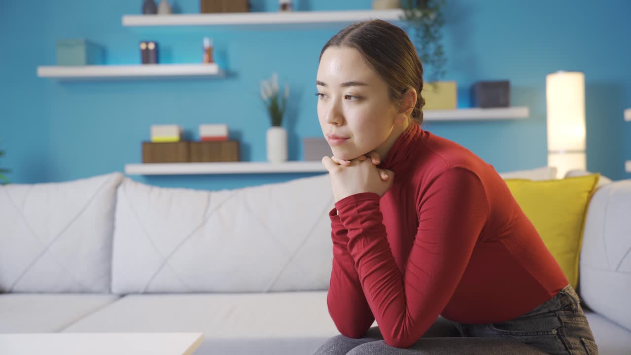 거실에 앉아 있는 사려 깊고 불행한 아시아 여성.