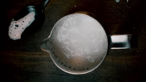 top-view-of-coffee-creamer-with-frothed-milk-bubbling-up-on-dark-background