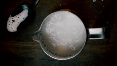 top view of coffee creamer with frothed milk bubbling up on dark background