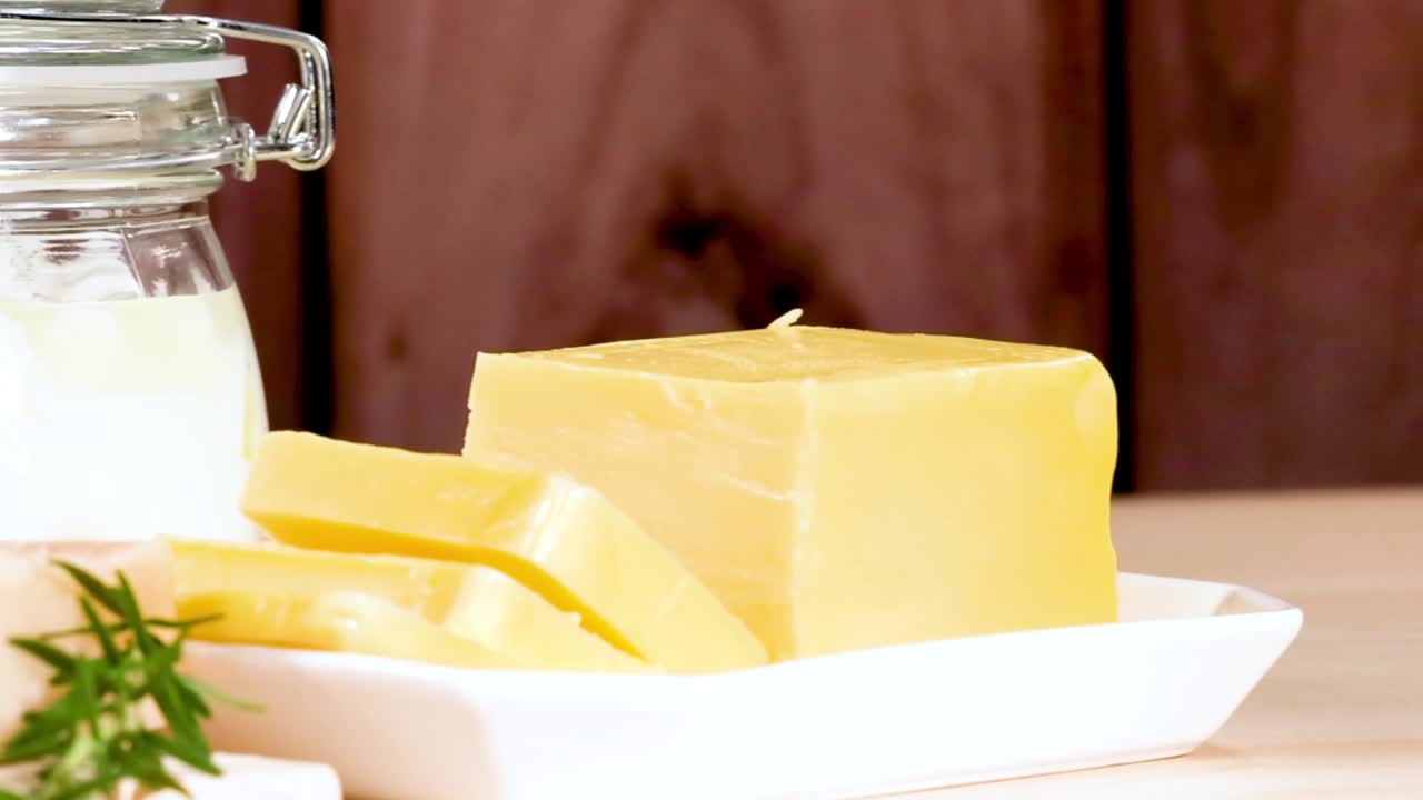 A variety of cheeses and dairy jars arranged on a wooden table with fresh herbs.