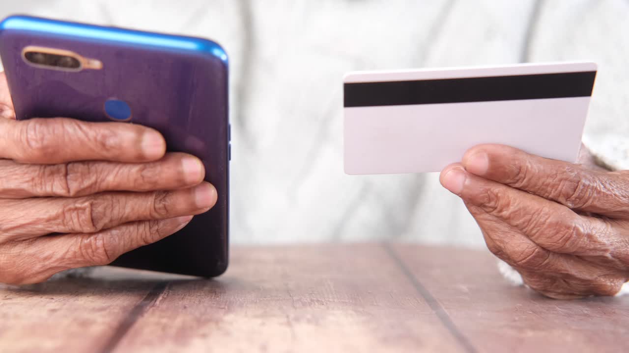 anciano que utiliza un teléfono inteligente y una tarjeta de crédito para el pago móvil