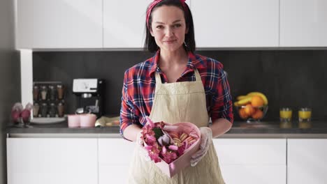 Frau-In-Schürze-Präsentiert-Schachtel-Mit-Makronenplätzchen,-Die-Mit-Blumen-Geschmückt-Sind