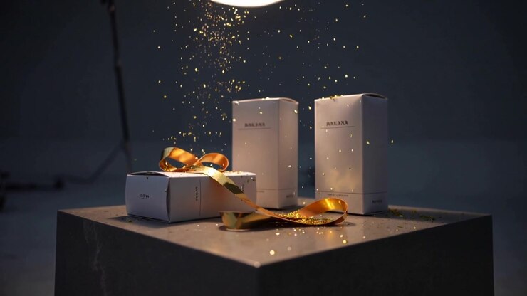 Falling gold glitter dusting three white boxes on studio pedestal, highlighting satin ribbon