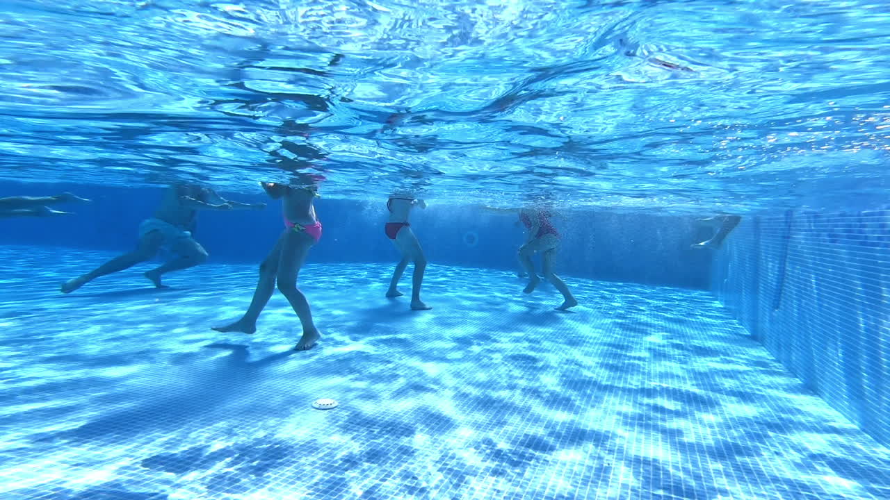 Underwater view of people's legs in the swimming pool. Legs of children and adults swimming inside the blue water.
