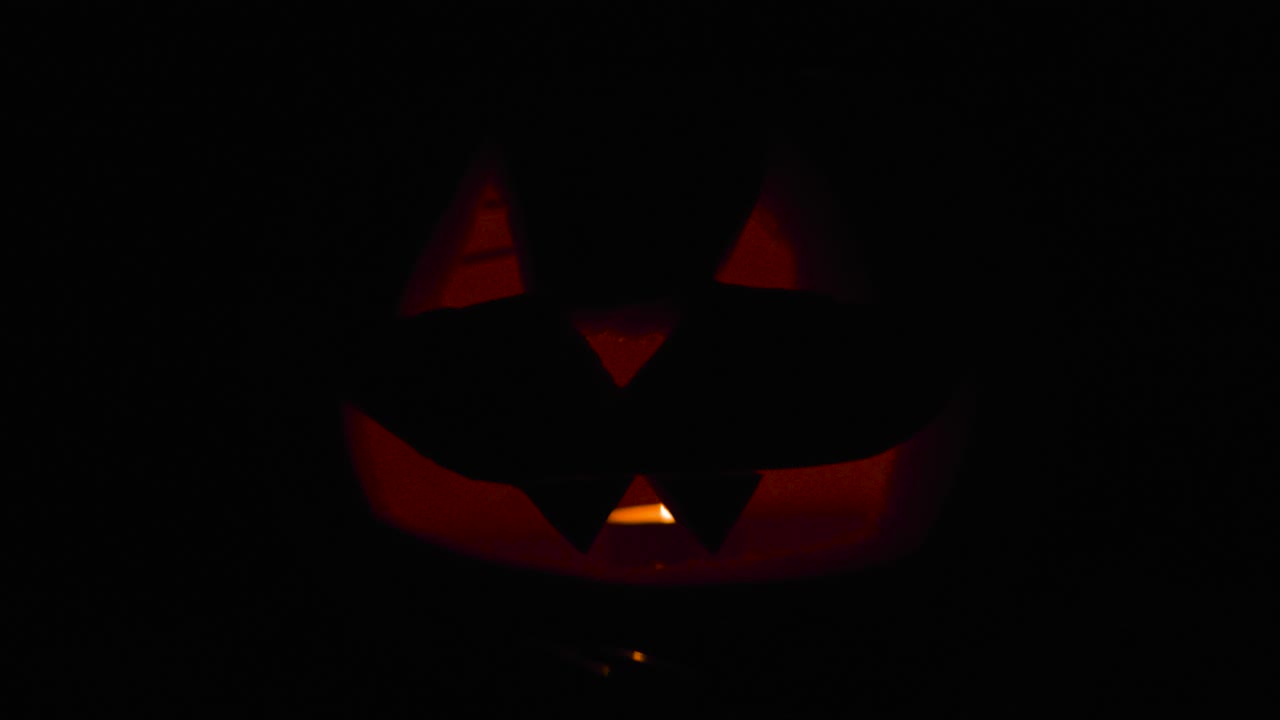 Happy Halloween 2 Jack O' Lanterns glowing in the dark wishing Happy Halloween: carved Pumpkin decorations with burning candles inside.