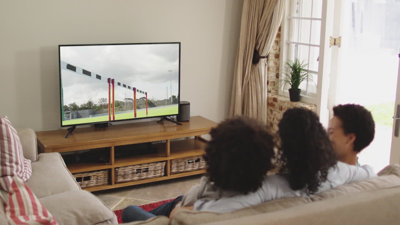Composizione: famiglia felice seduta a casa insieme che guarda la corsa a ostacoli in TV.