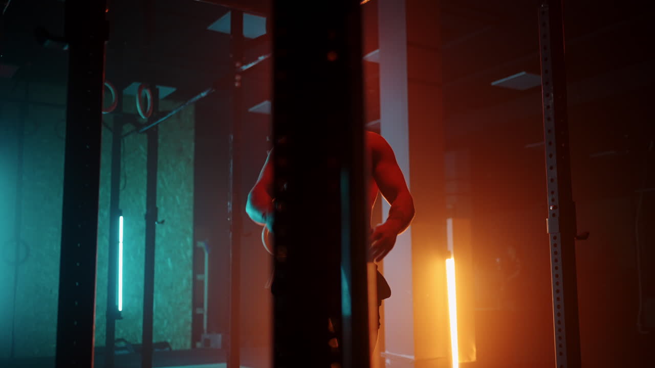 Uomo fitness che esegue un esercizio di arrampicata su corda in palestra al rallentatore. Luce al neon arancione e blu. Uomo che si allena in palestra arrampicandosi su una corda.