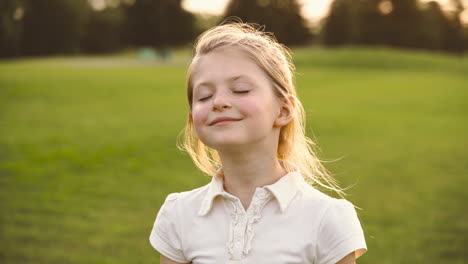 retrato de una linda niña rubia con los ojos cerrados sonriendo rodeada de burbujas de jabón en el parque 3