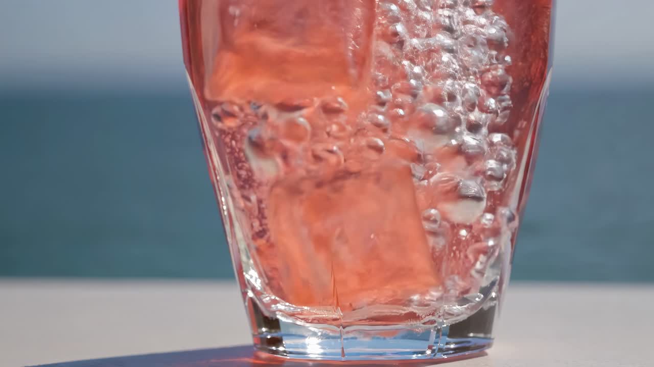 Refreshing beverage in clear glass with ice cubes and bubbles, showcasing dynamic movement and vibrant colors against a serene background, capturing the essence of summer enjoyment