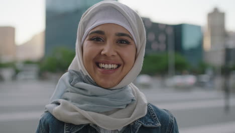 portrait of young independent muslim woman looking at camera smiling cheerful wearing hajib headscarf in urban city at sunset