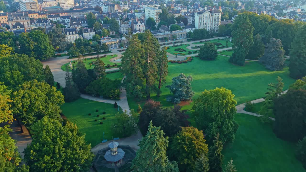 Drone shot moving forward over Parc du Thabor in Rennes, showing paths, gardens, a fountain, and the city illuminated by sunrise light