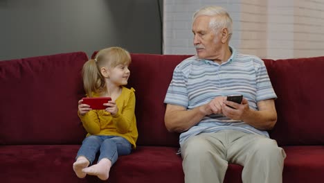 Senior-grandfather-with-child-girl-granddaughter-using-digital-mobile-phone,-playing-games-at-home