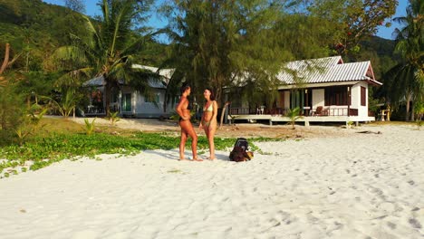 paradise vacation destination on tropical island with beach cabins near white sand where two beautiful girls in bikini sunbathe in bali