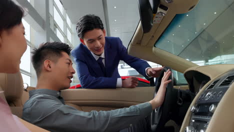 couple with attractive auto dealer in a suit presenting new car model to his client