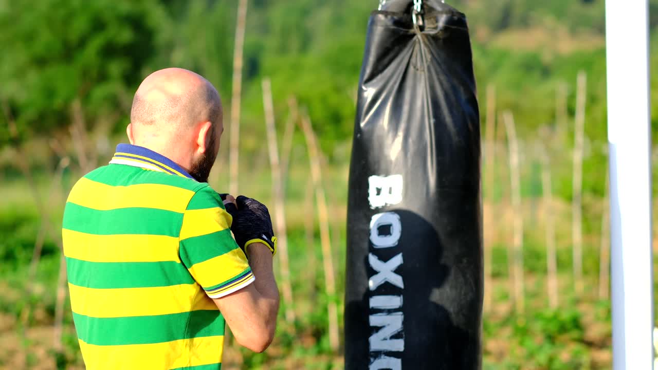 o atleta treina com um saco de boxe preso a um aro de basquete em câmera lenta na natureza