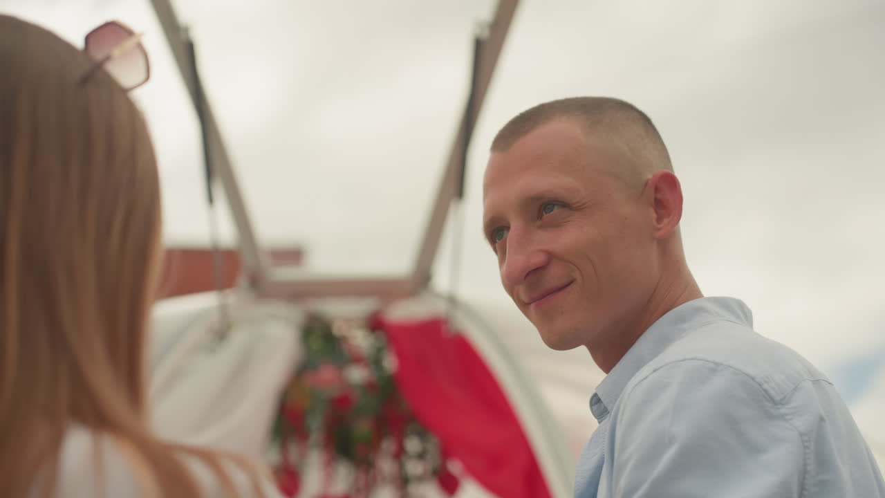 Scambio intimo di promesse all'aperto sotto un arco fiorito. Uno sposo bianco e il suo partner si scambiano teneri sorrisi e sussurrano promesse sotto un drappeggio rosso e fiori sospesi; primi piani spontanei catturano sguardi affettuosi.