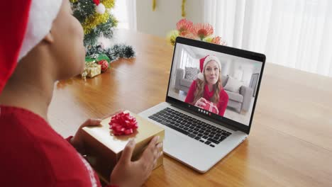 Mujer-Afroamericana-Con-Sombrero-De-Santa-Usando-Una-Computadora-Portátil-Para-Una-Videollamada-Navideña-Con-Una-Mujer-En-La-Pantalla