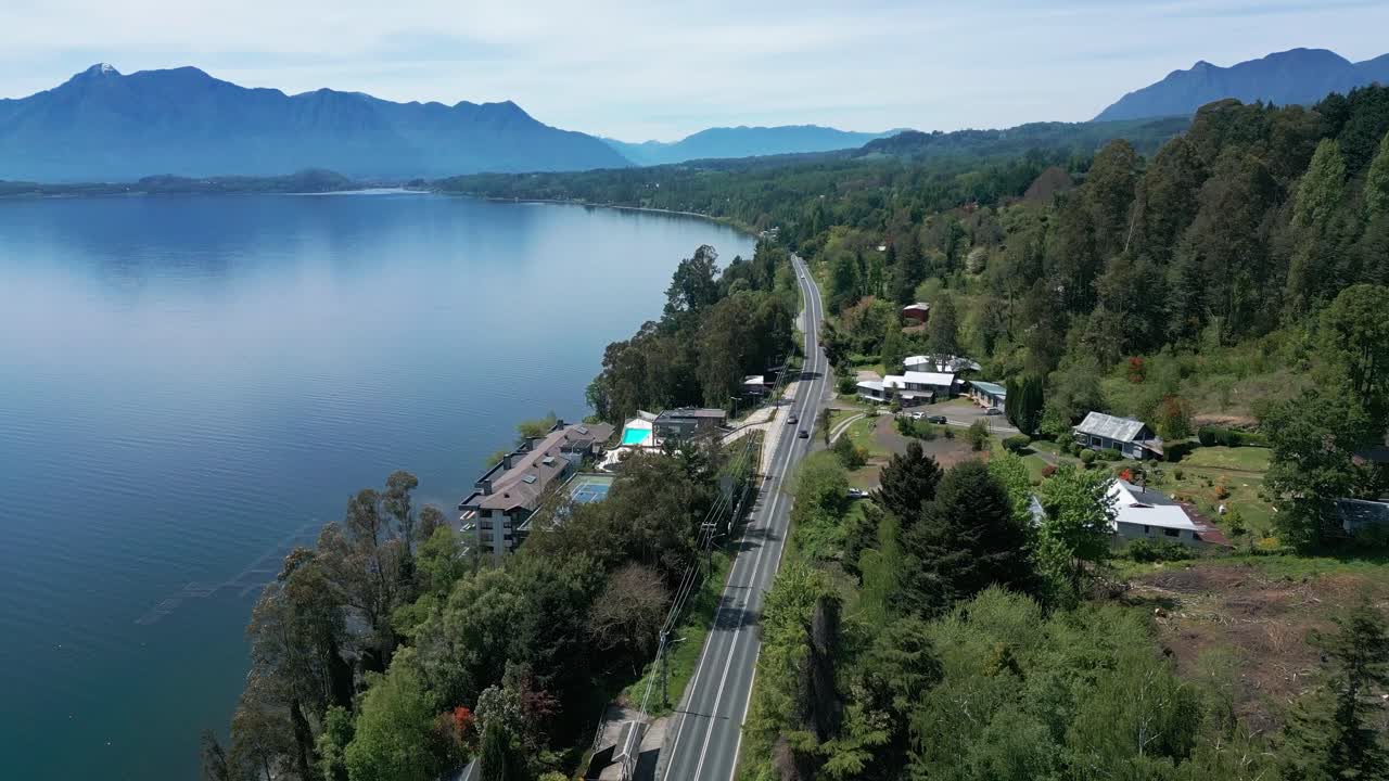 Drone Shot of Cars Driving Along a Scenic Road Beside Lake Villarrica in Southern Chile, Lined with Lush Forest and Mountain Views in the Background