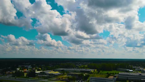 aerial drone hyperlapse of sunset and day time sunny sky above a urban city or town area with white clouds moving fast in blue sky. traffic and small houses and warehouses visible below on streets