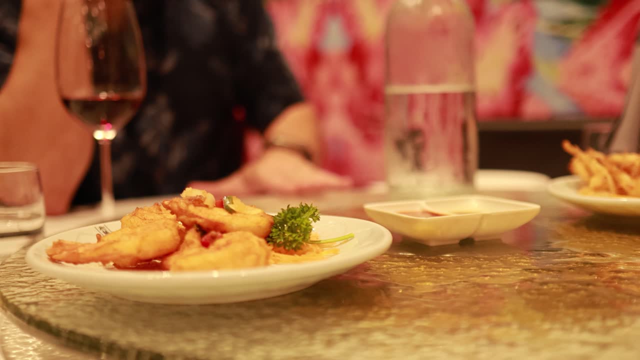A lazy Susan spins on a restaurant table with dishes, wine, and colorful decor, creating a lively dining atmosphere