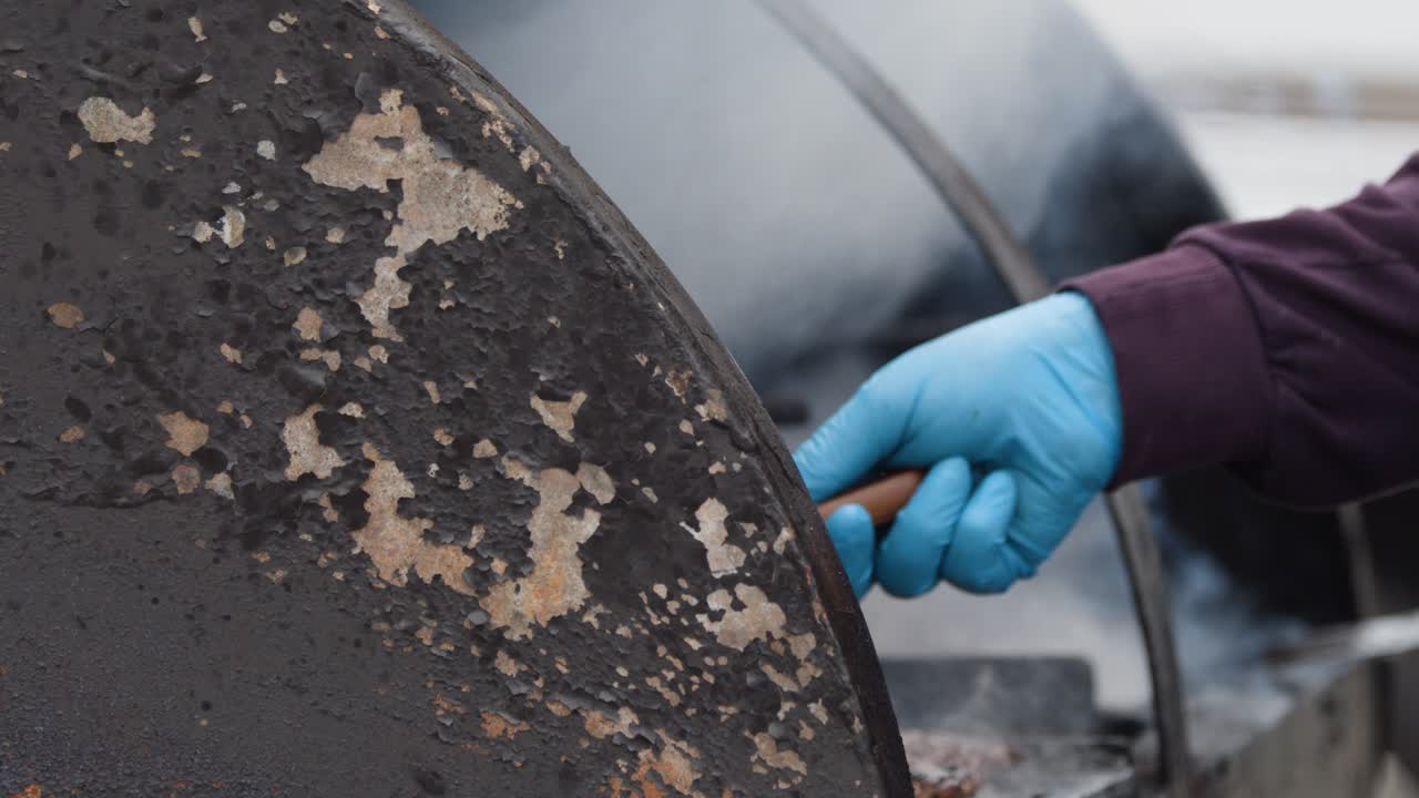 Gloved hand turns meat on large smoky grill, overcast daylight, shallow focus, steady camera