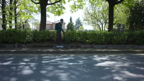 disparo ancho de un hombre montando un scooter eléctrico en el camino por el parque, día soleado, estático