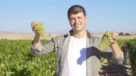 joven agricultor sosteniendo un racimo de uvas y mirando a la cámara.