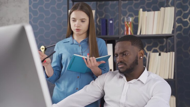 Two multiethnic office workers discussing financial market data using computer. Different races and ethnicity concept.
