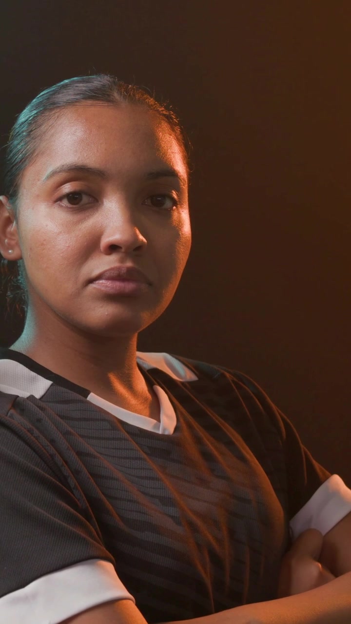 Vídeo vertical: Modelo feminina cruzando os braços, virando-se para a câmera, movendo-se com iluminação de contorno destacando roupas esportivas