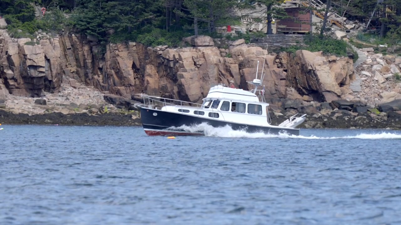 Perahu motor melaju di dekat pantai berbatu di Mount Desert, Maine.