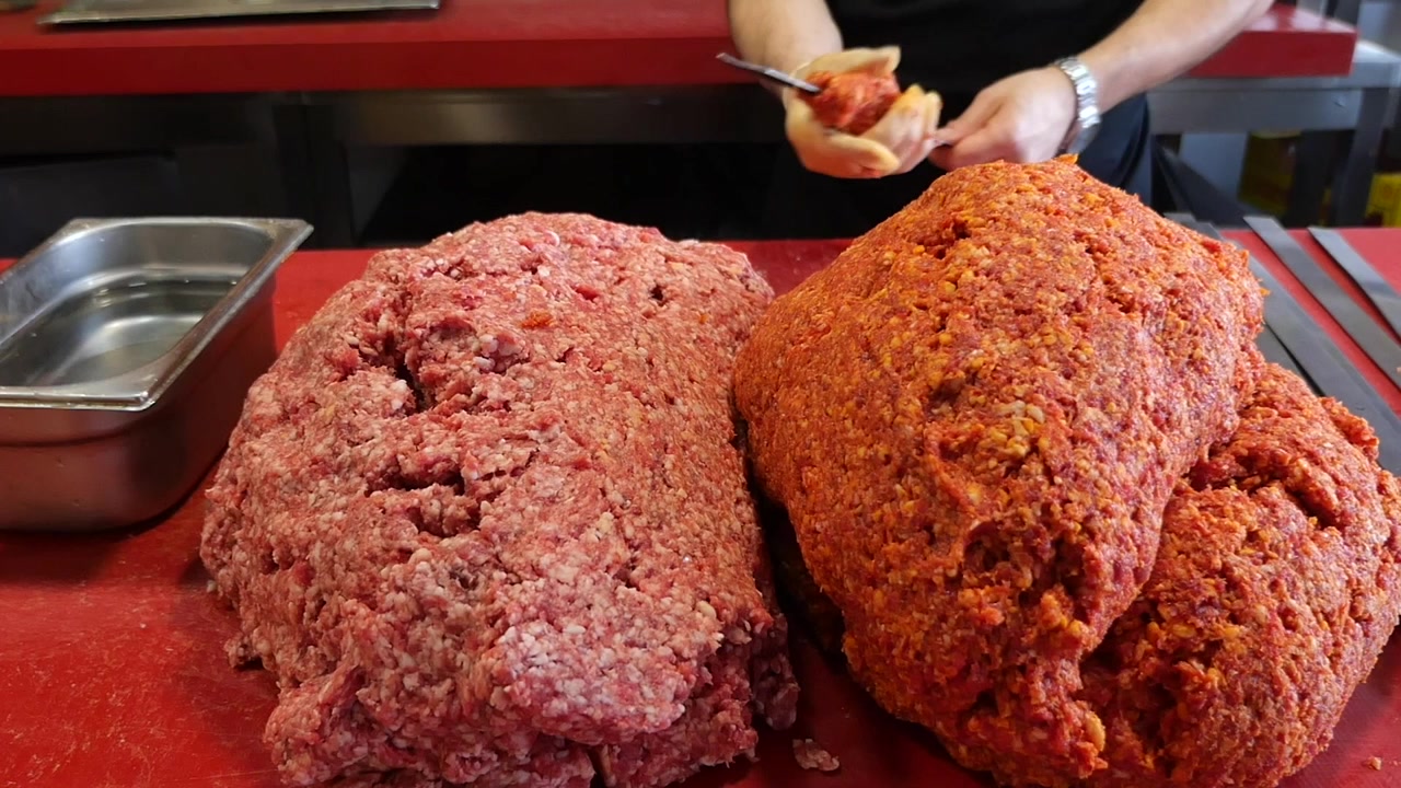 Macellaio che prepara spiedini di carne macinata in una cucina professionale.